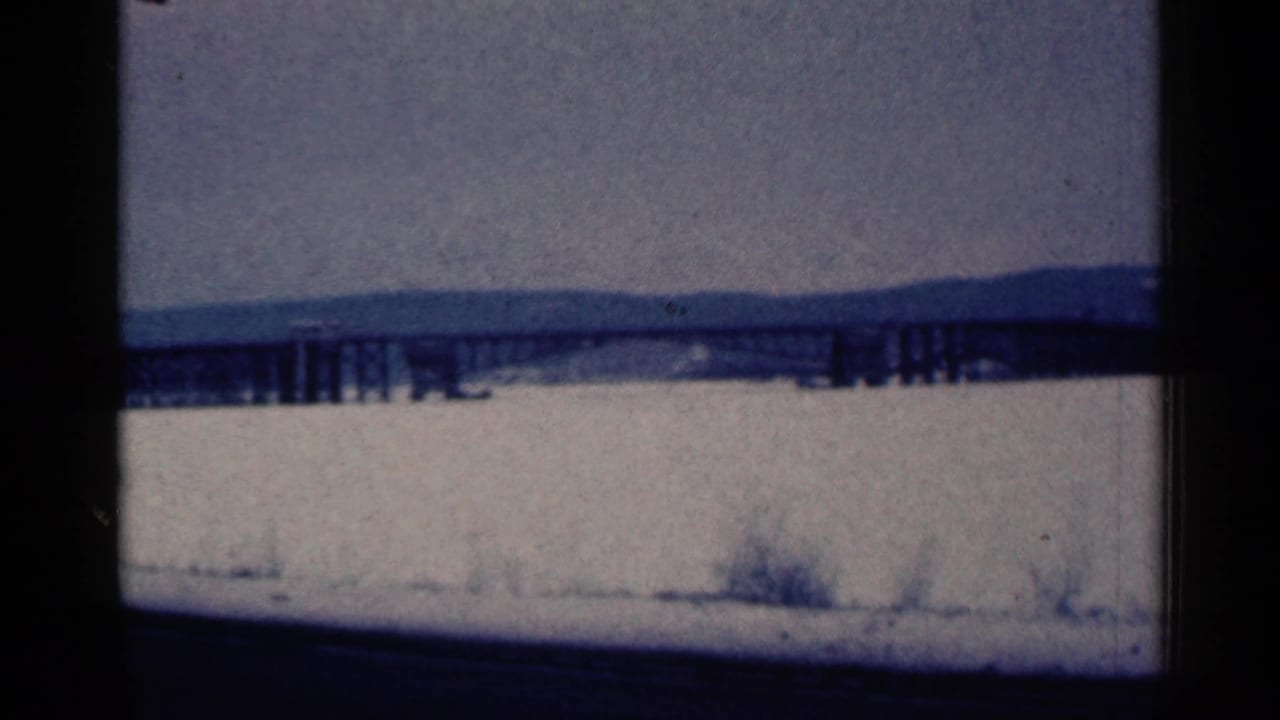 Snowy roadside view with a long bridge or trestle across a pale frozen landscape.