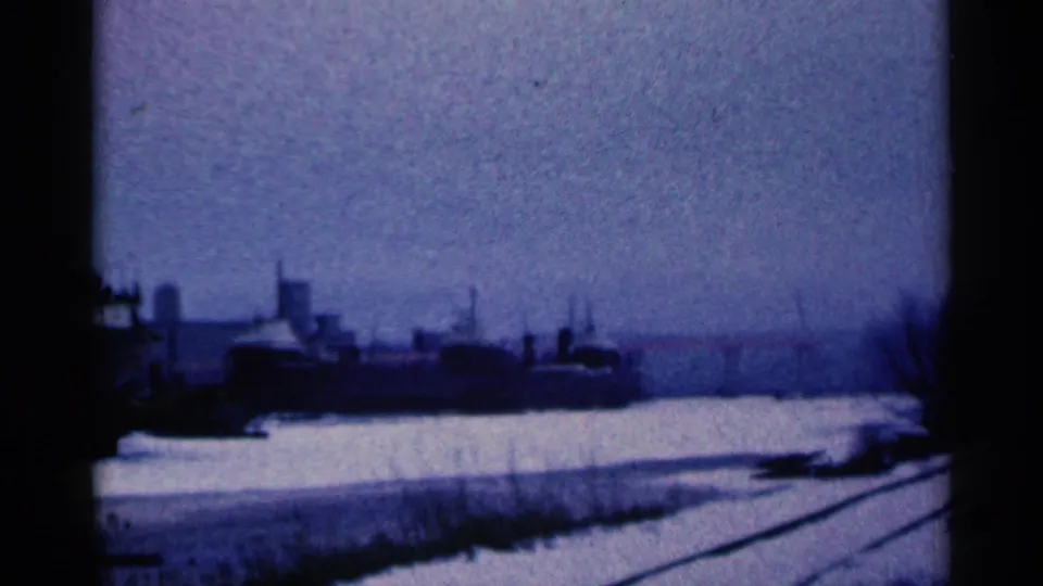 1961 Duluth, Minnesota frame showing a snowy industrial waterfront area with rail tracks and a large vessel or industrial structure.