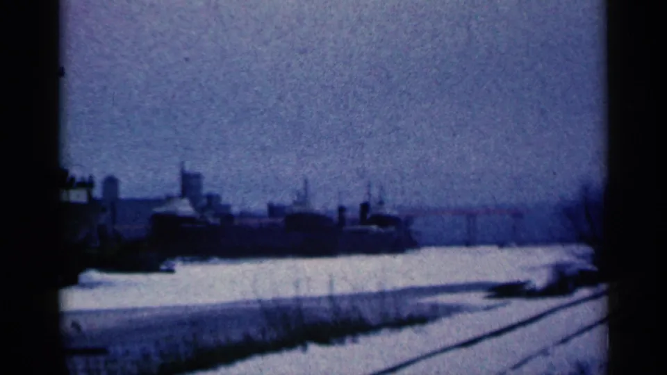 Duluth, Minnesota 1961 home-movie frame showing snow-covered rail lines and distant industrial buildings in winter.