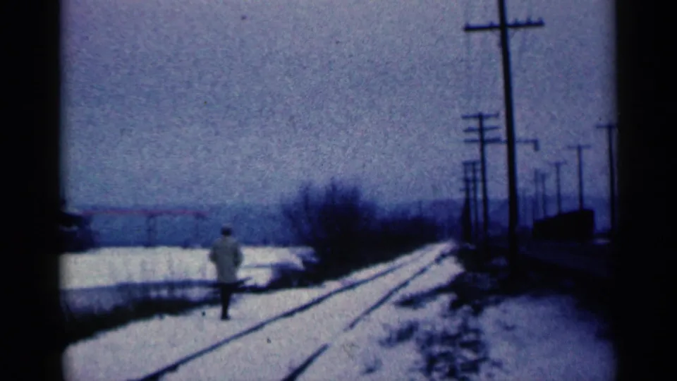 The distant man continues along the snowy Duluth rail corridor, framed by utility poles and a cold industrial horizon.