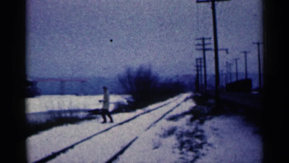 A distant pedestrian in a light coat crosses near snow-covered tracks in a 1961 Duluth industrial winter scene.