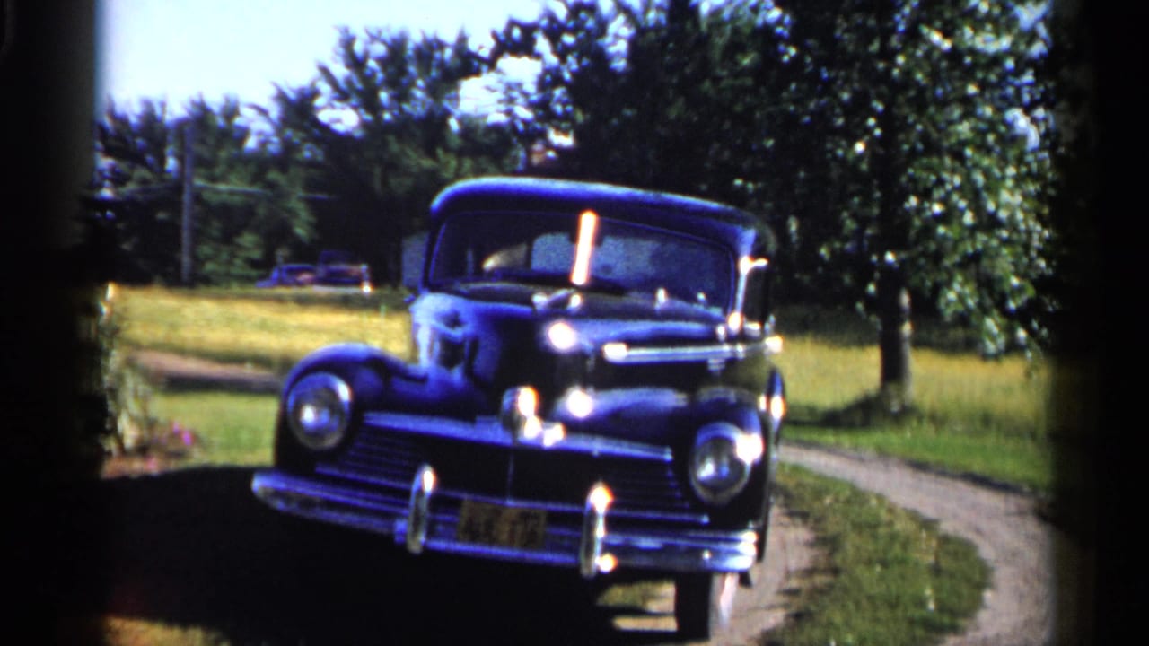 A black mid-century sedan sits on a curved rural drive in Duluth, Minnesota, in 1961 home-movie footage.