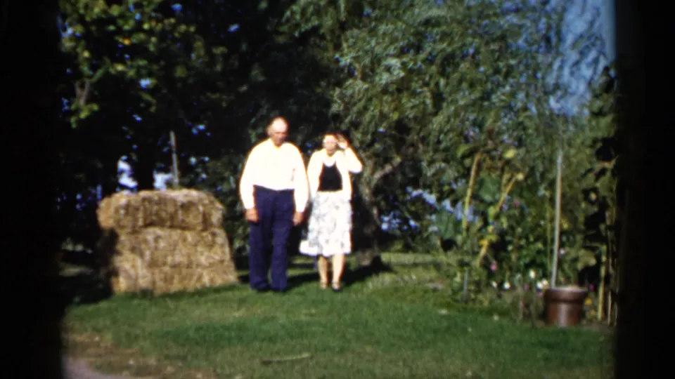 The older couple remains near the hay bale in the Duluth backyard, with the woman raising a hand as if waving toward the camera.
