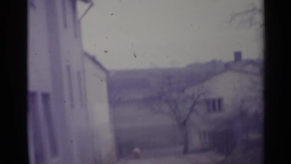 1961 Spain 8mm frame showing white residential buildings, bare branches, and a distant hillside in soft, purple-tinted focus.