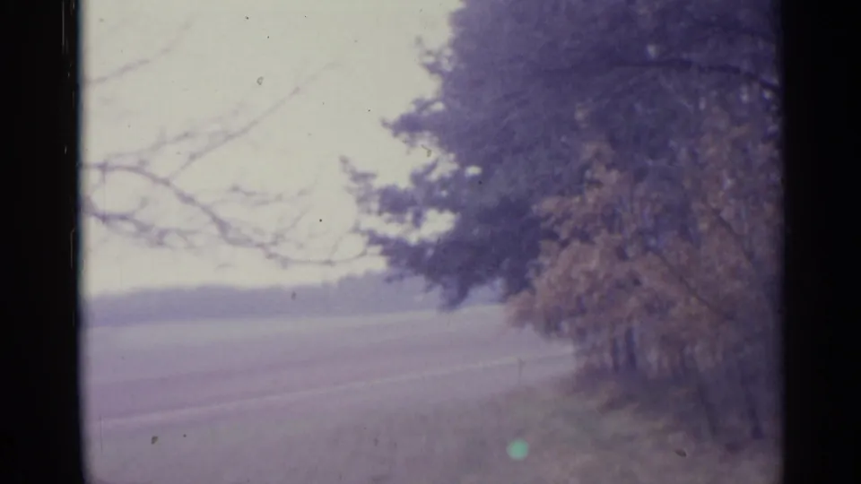 1961 Spain 8mm frame showing a quiet rural road or path with trees along the edge and distant open land.