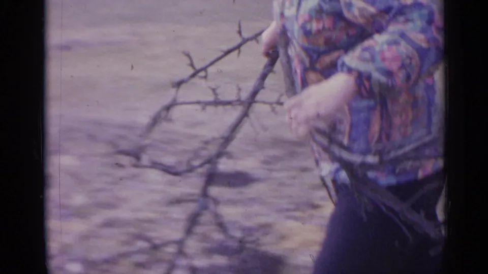 The frame centers on the fallen branches being carried, with the woman partly cropped at the edge of the 8mm frame.