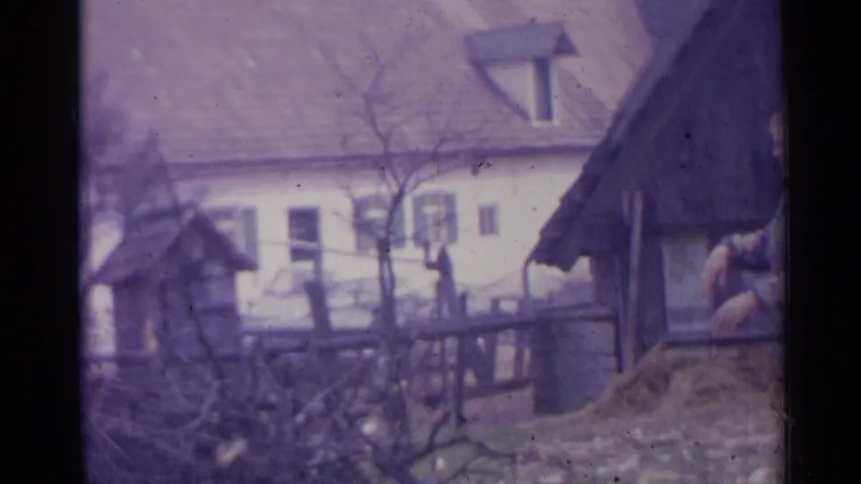 A wider 1961 Spain farmstead view shows a tiled-roof house, bare trees, fencing, yard debris, and part of a person at the edge.