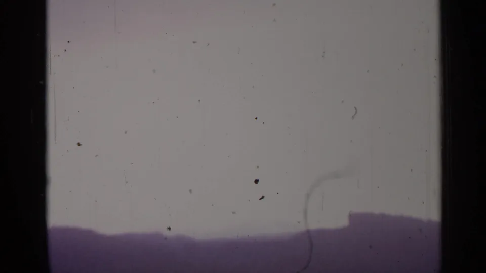 A hazy Spanish rural horizon appears beneath a pale sky as the camera shifts away from the farm structures.