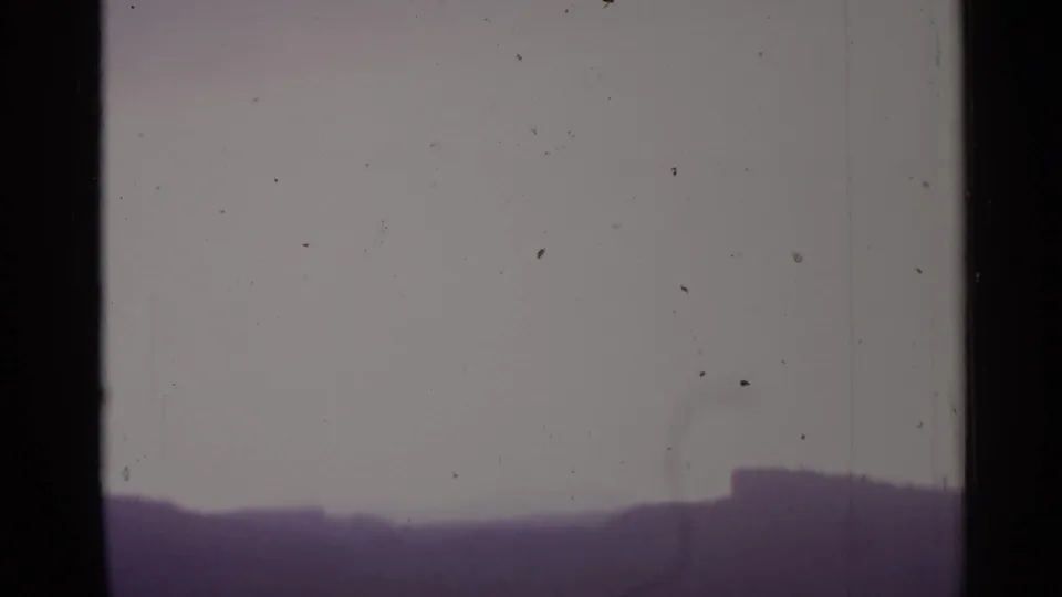 A soft 8mm view of a distant skyline or ridge under a pale sky, with visible dust and edge framing.