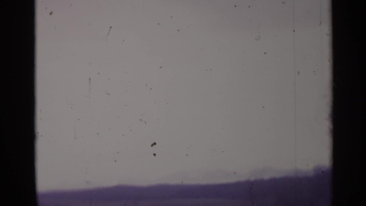 1961 Spain 8mm frame showing a muted elevated view of low hills with a bare tree at the edge and visible film dust.
