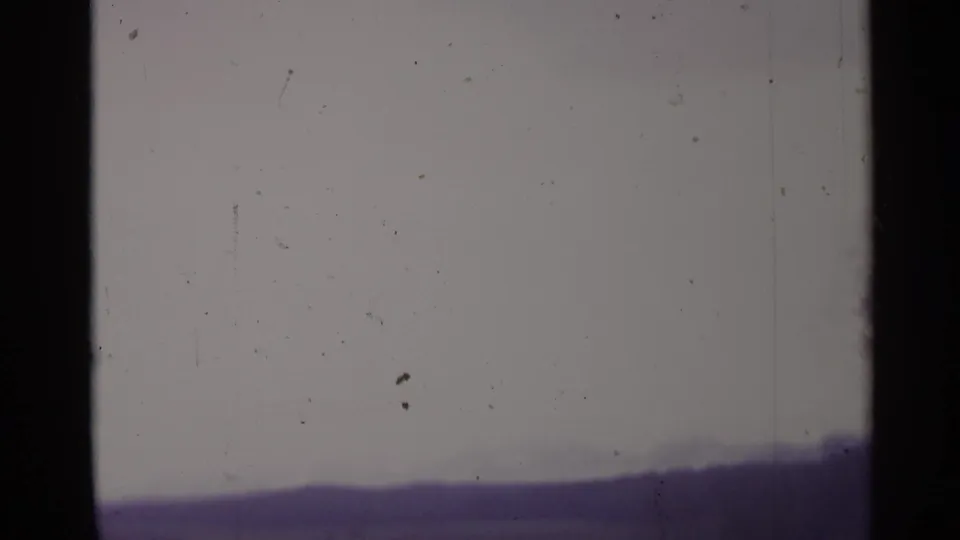 1961 Spain 8mm frame showing a muted elevated view of low hills with a bare tree at the edge and visible film dust.