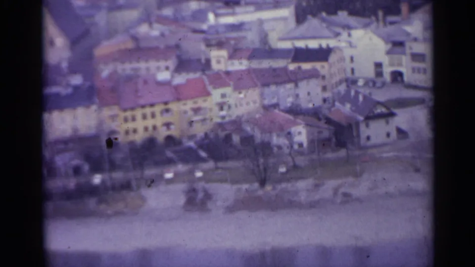 1961 Spanish town exterior with colorful facades, red-tiled roofs, bare trees, parked cars, and a deserted-looking street below.