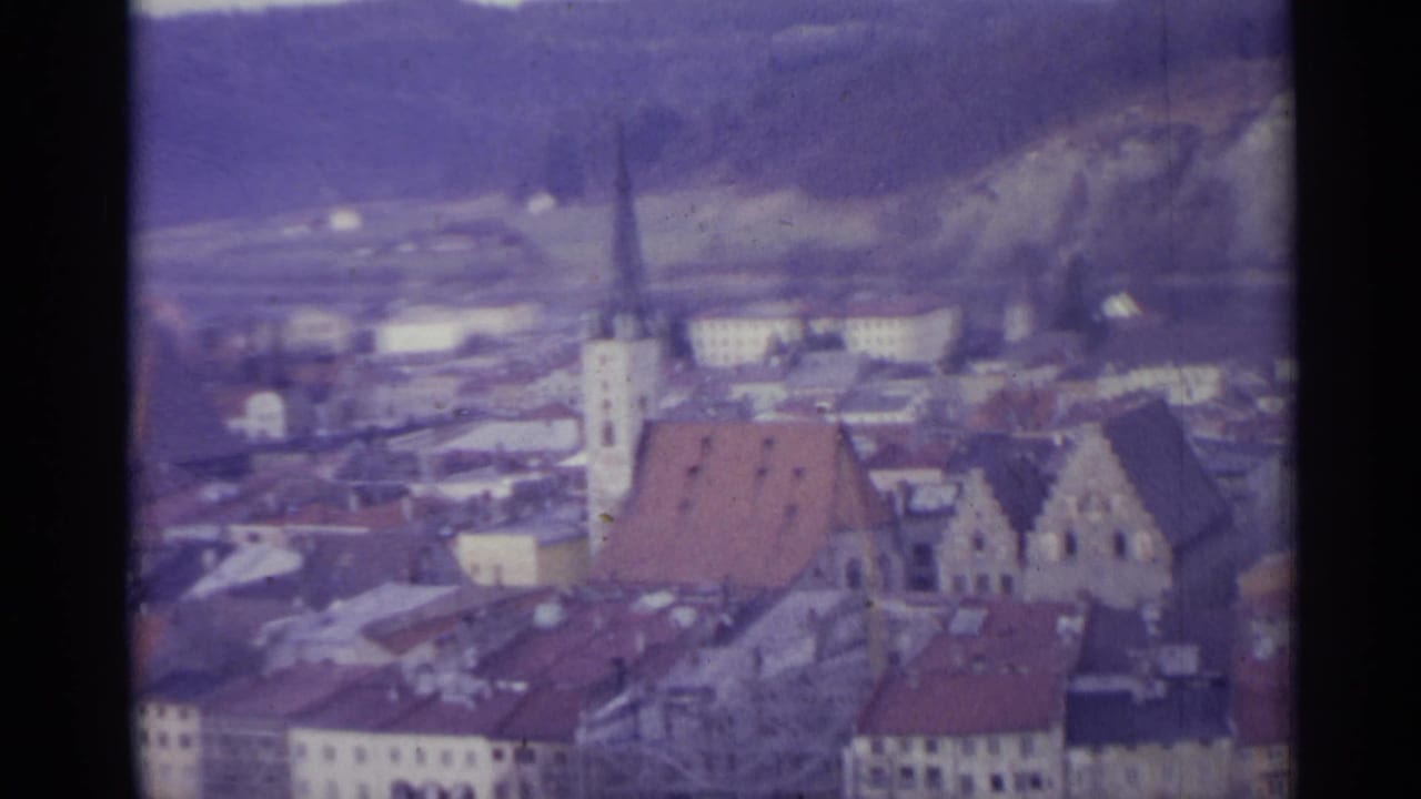 Church tower and red-roofed buildings seen from above with hills behind the town.