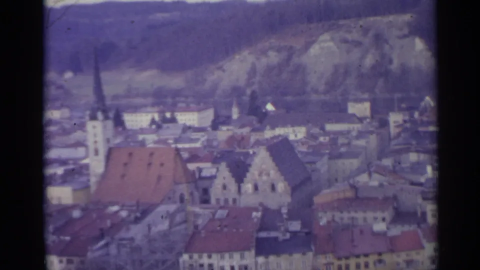 1961 Spain 8mm frame showing rooftops, a church tower, dense town blocks, and hillside terrain beyond.