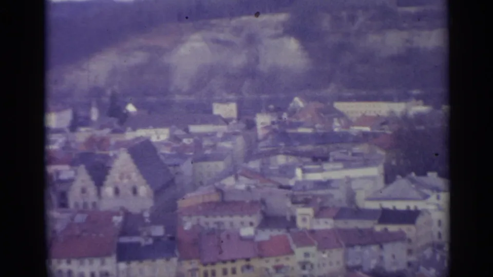 1961 Spain 8mm frame looking over clustered rooftops, pale town buildings, a church structure, and hills beyond.