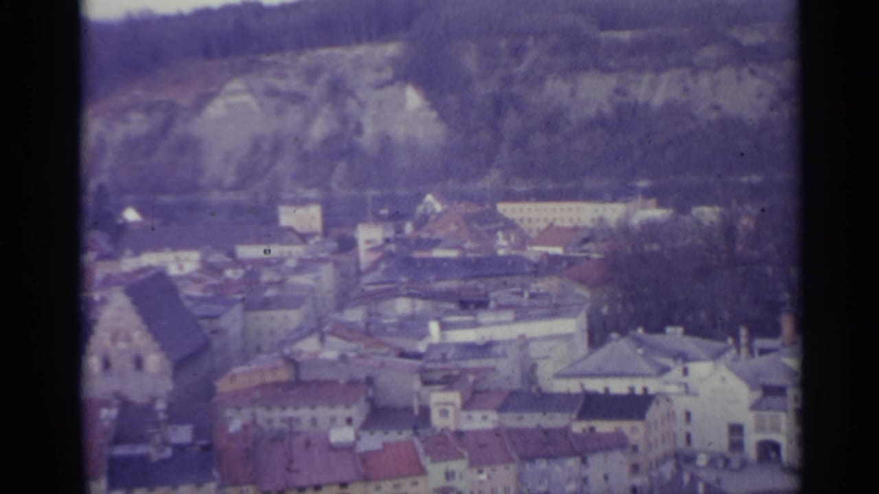 Elevated view of a village with red roofs below rocky hills.