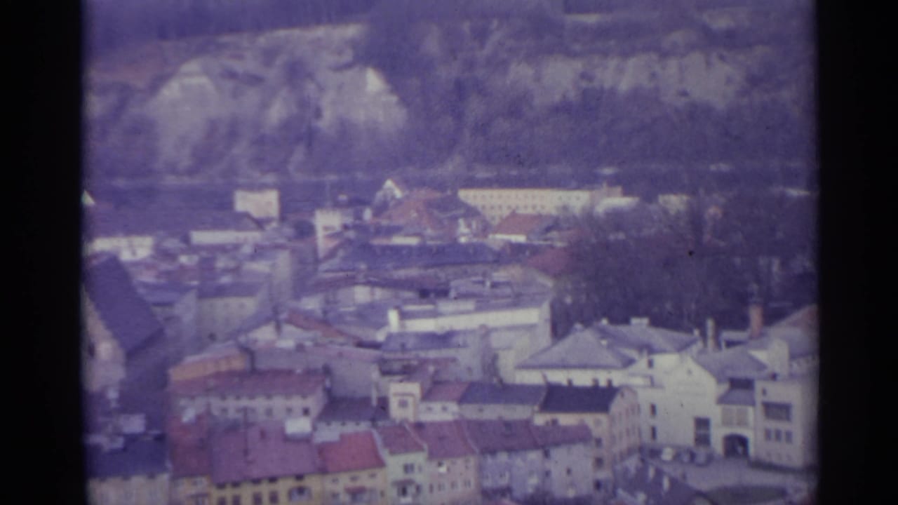 Village buildings and rooftops viewed from above with hills behind.