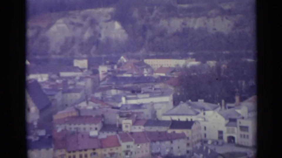 Elevated 1961 Spain view of varied town buildings, red roofs, and a wooded rocky slope in the background.