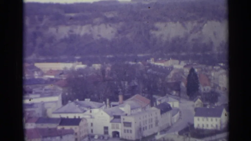1961 Spain home-movie view of pale village buildings, red roofs, bare trees, and wooded hills in soft 8mm color.