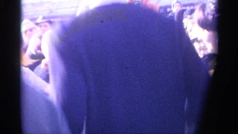Spain 1961 home-movie frame with a foreground figure in blue clothing and spectators or dancers visible in the background.