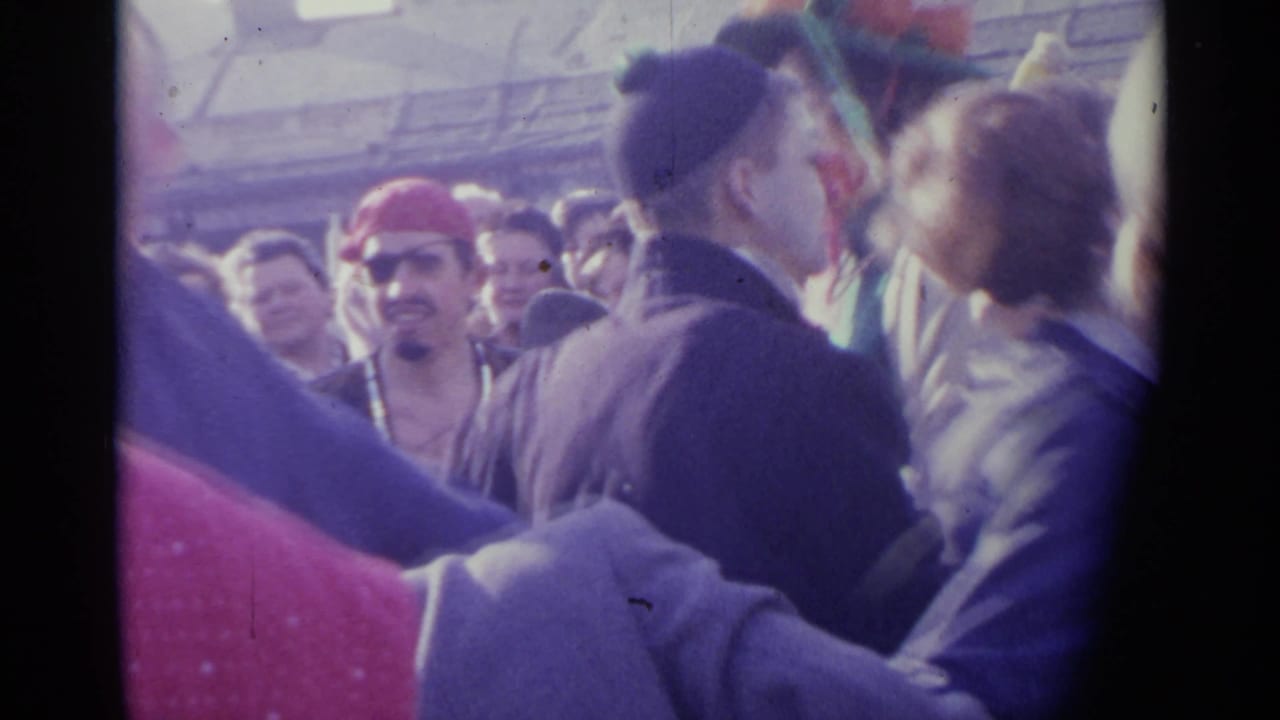Crowded outdoor dance scene with adults linking hands and a man in a red hat at left.