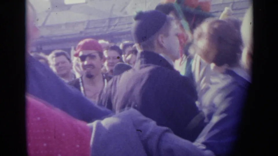 1961 Spain 8mm frame showing adults in a crowded street dance, with linked hands, close faces, and a man wearing a red hat near the left side.