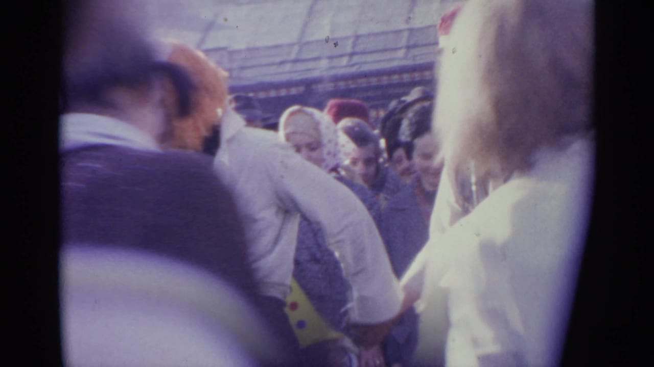 1961 Spain home-movie frame from inside a dense public crowd, with adults facing different directions and the view partly obscured by nearby shoulders.