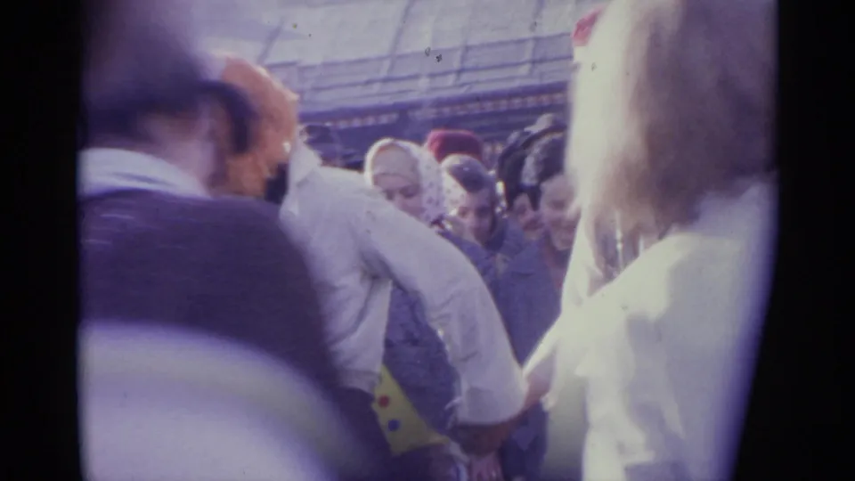 1961 Spain home-movie frame from inside a dense public crowd, with adults facing different directions and the view partly obscured by nearby shoulders.