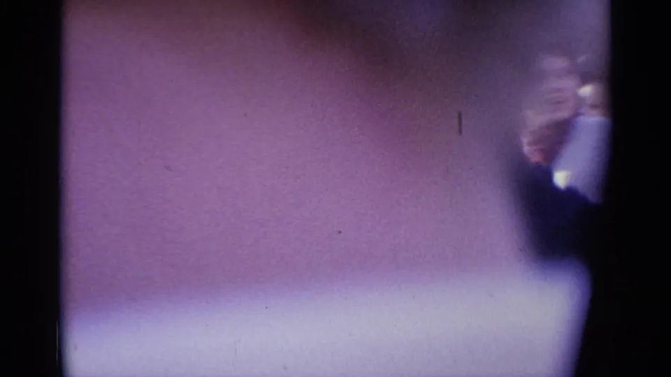 Obscured 8mm frame from the same 1961 Spain crowd scene, with soft purple color cast and only a partial glimpse of participants at the edge.