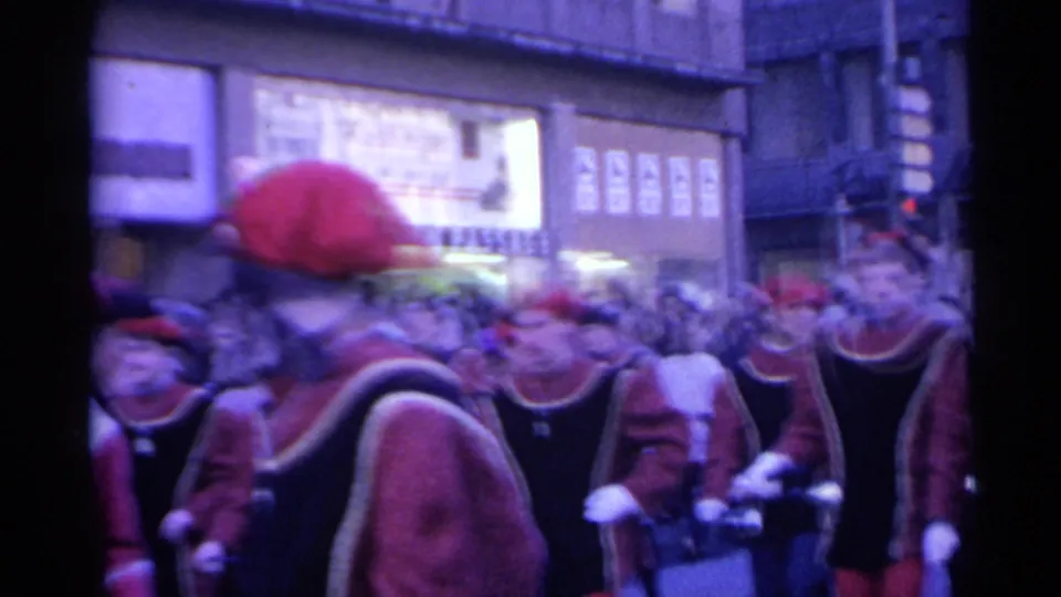 1961 Spain home-movie frame showing red-hatted parade participants moving through a dense urban crowd.