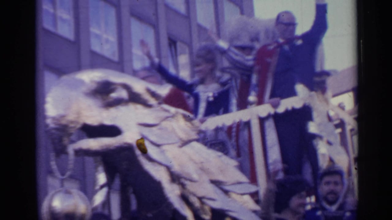 Close 1961 Spain parade frame showing a golden eagle ornament, a waving formal figure, attendants, float railings, and spectators at street level.