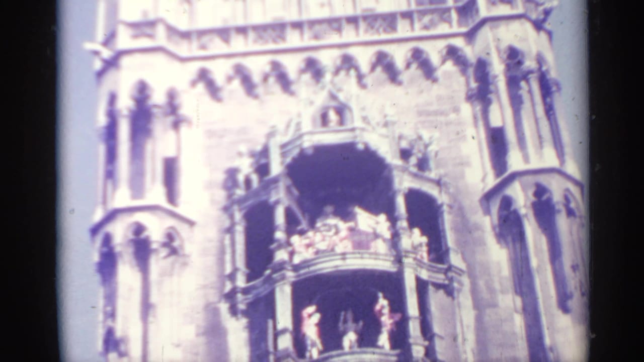 Soft 8mm frame of an ornate building facade in Spain with people visible on a balcony during the parade setting.