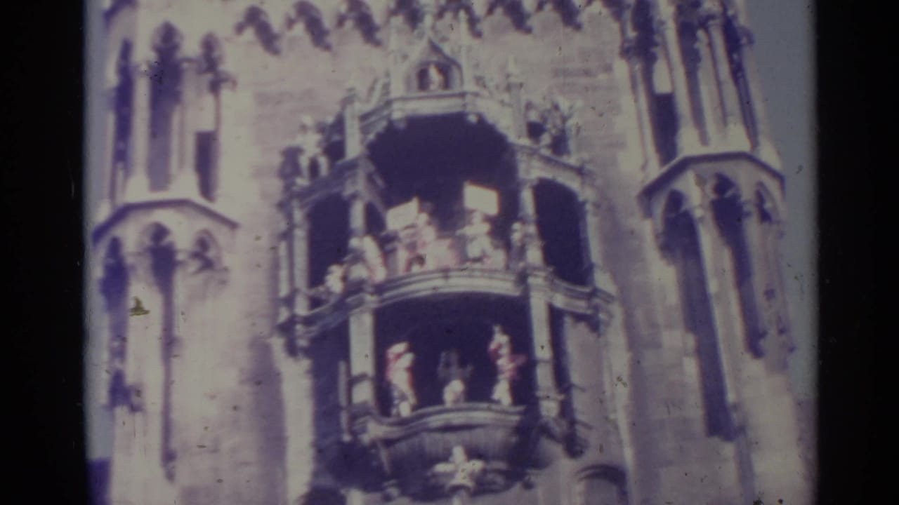 1961 Spain 8mm frame of balcony figures on an ornate Gothic-style tower facade, seen through soft focus and faded color.
