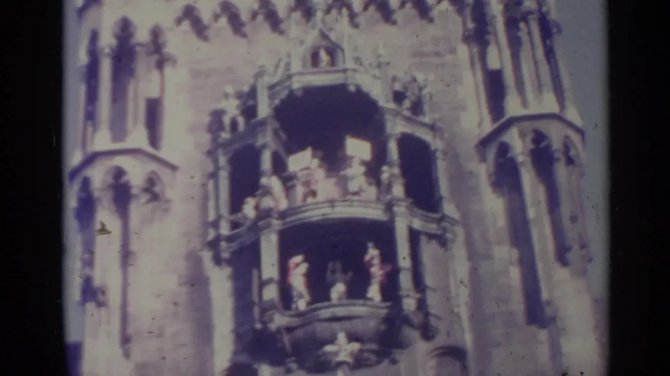 1961 Spain 8mm frame of balcony figures on an ornate Gothic-style tower facade, seen through soft focus and faded color.