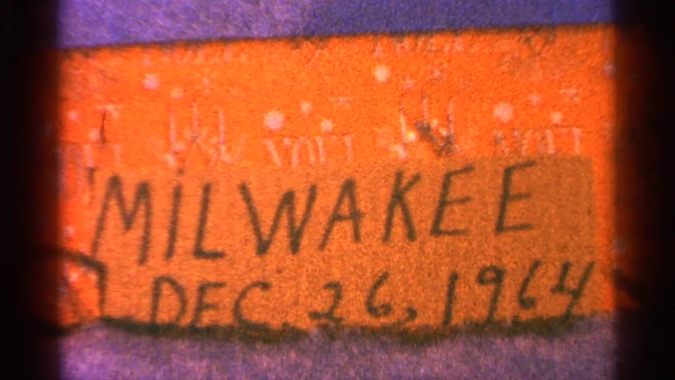 Soft 8mm close-up of an orange handwritten Milwaukee date label with purple border and visible film grain.