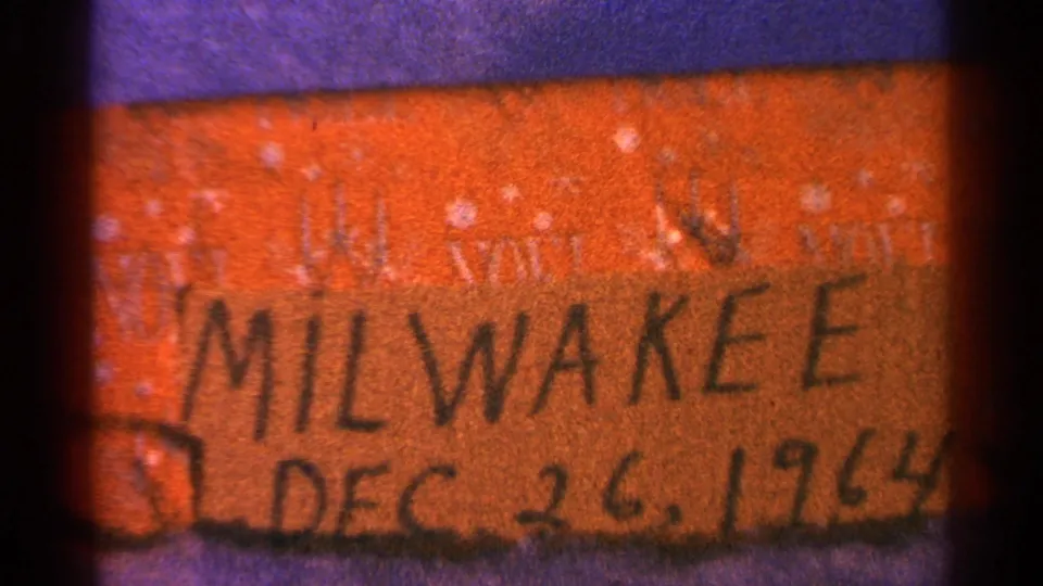 Grainy 8mm view of the orange Milwaukee label, with the date along the lower edge and purple border below.
