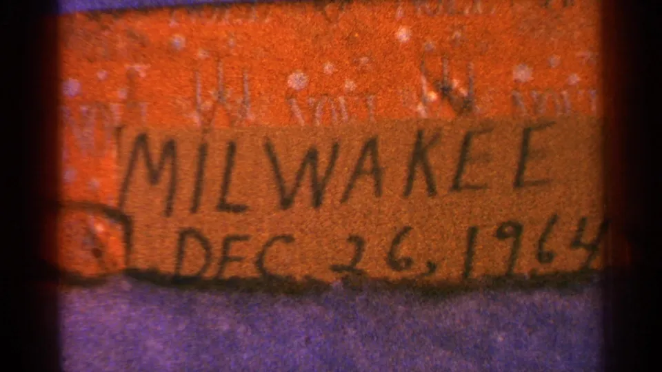 Final 8mm frame of the orange handwritten Milwaukee date label, cropped by dark film edges and grain.