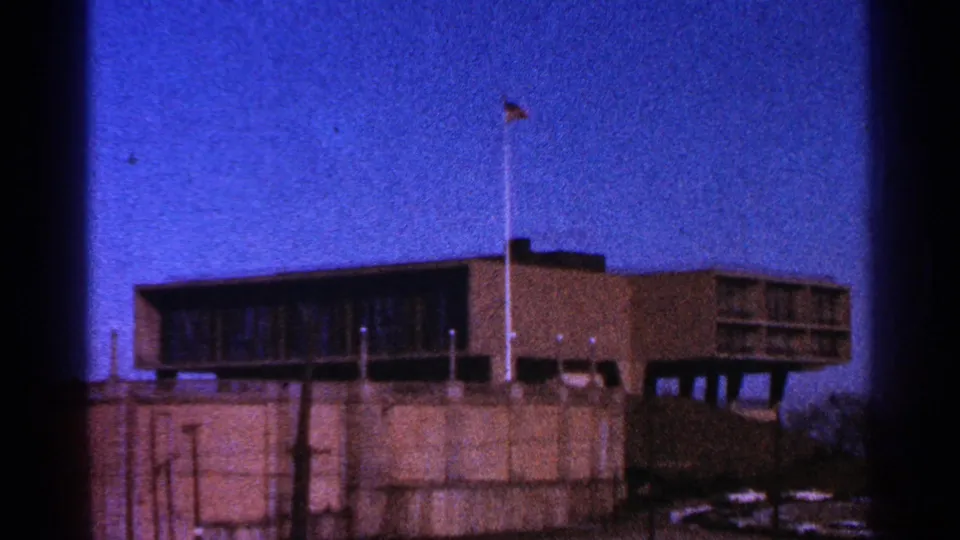 1964 Milwaukee 8mm frame of a raised brown building with a flagpole, concrete base, streetlights, and saturated blue sky.