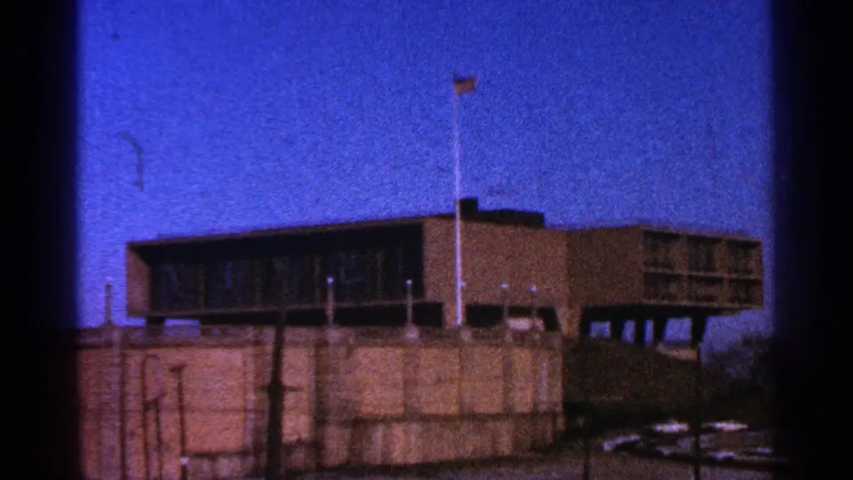 1964 Milwaukee frame showing the brown modernist building, flagpole, dark window band, concrete foreground, and visible 8mm gate edge.