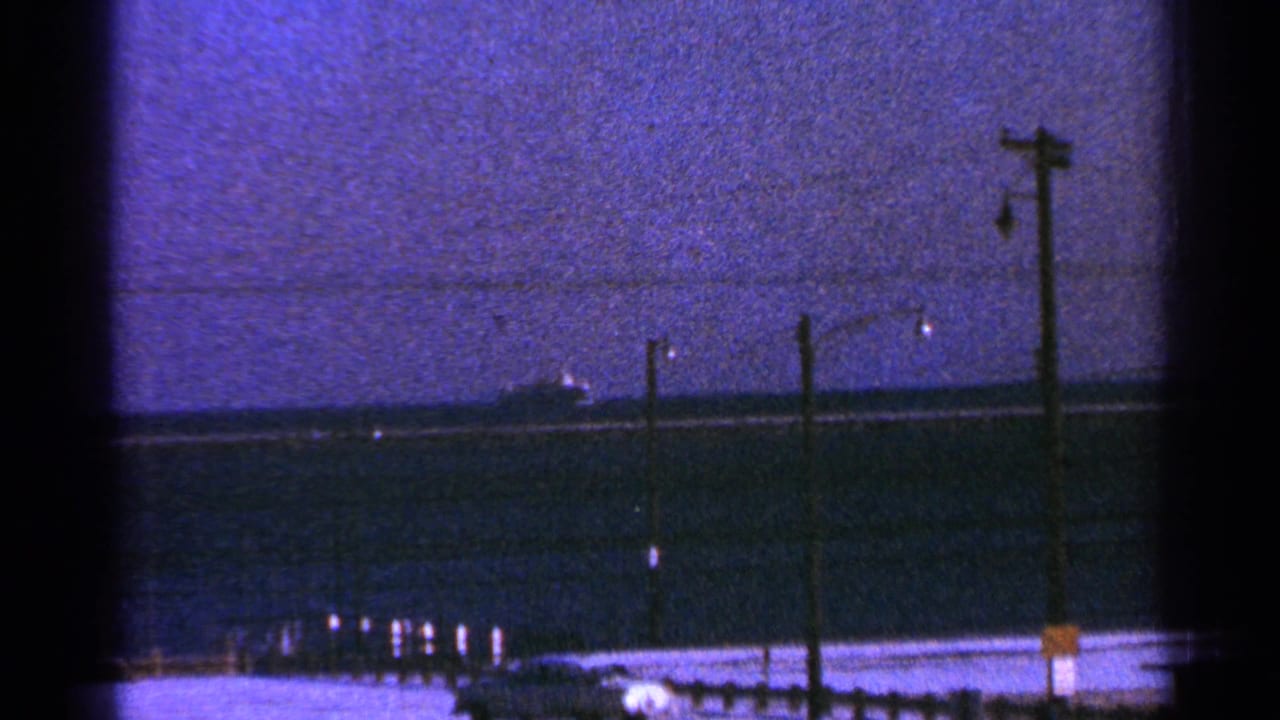 1964 Milwaukee-associated 8mm frame showing a distant ship beyond a shoreline with utility poles and a darkening sky.