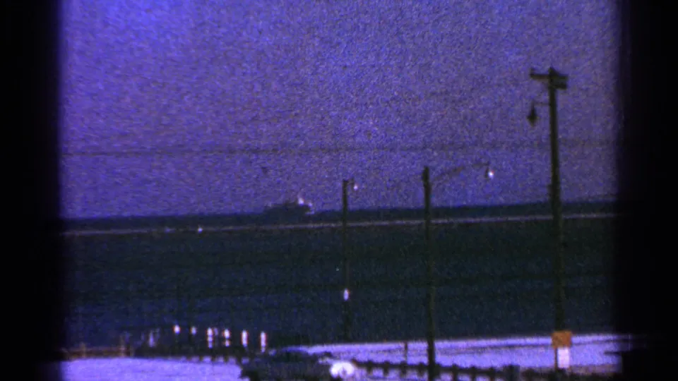 1964 Milwaukee-associated 8mm frame showing a distant ship beyond a shoreline with utility poles and a darkening sky.