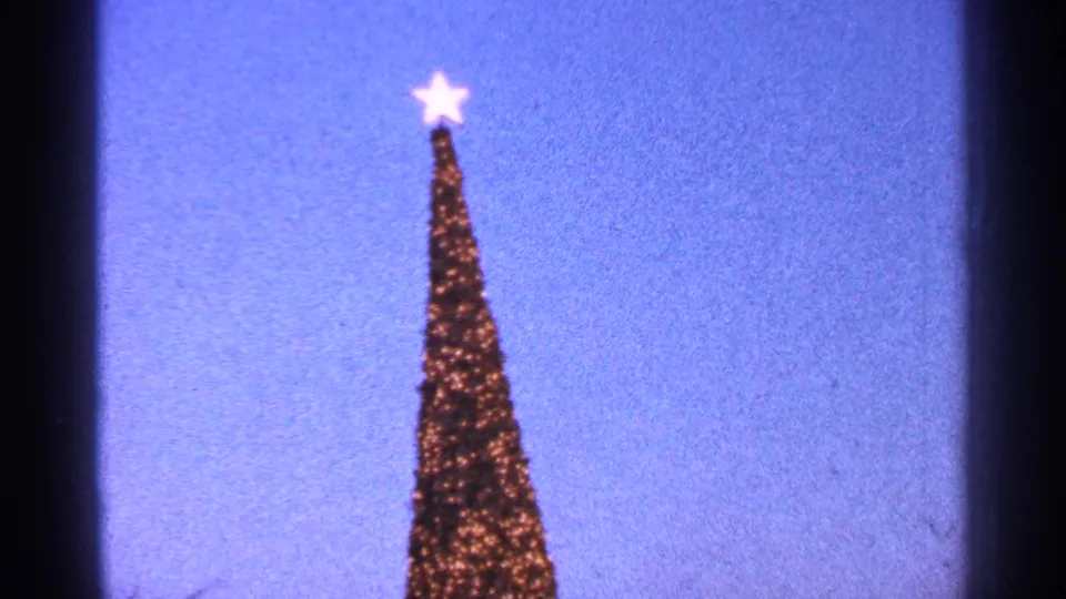 1964 Milwaukee 8mm frame showing the upper section of a tall illuminated Christmas tree and star against twilight sky.