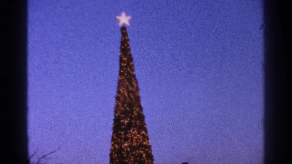 1964 Milwaukee home-movie frame with the lit tree top and glowing star centered against deep blue sky.