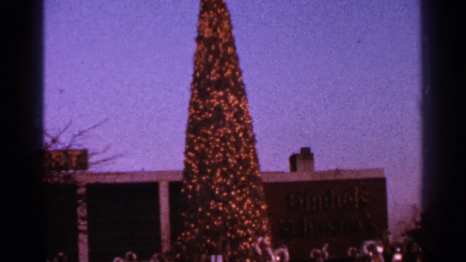 1964 Milwaukee frame showing a tall decorated Christmas tree, partial Gimbels signage, and small holiday display figures near the base.