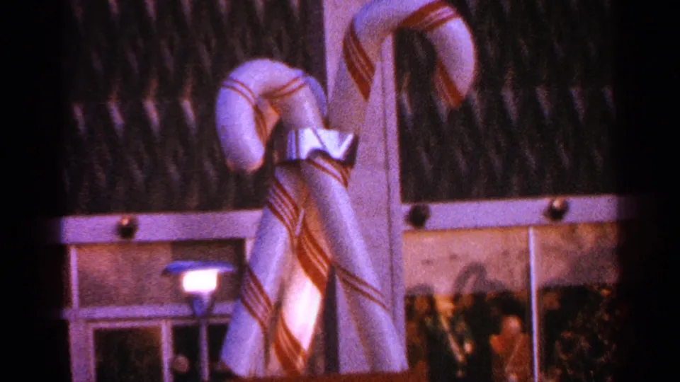 Closer 1964 Milwaukee frame showing large candy cane decorations with bows and light trim near building windows, with people visible at the lower edge.