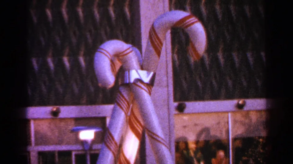 1964 Milwaukee home-movie frame of red-and-white candy-cane decorations, a reflective bow, and shadowed glass behind them.