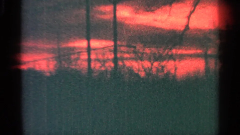 1964 Milwaukee 8mm frame with a saturated red-orange sky, silhouetted trees, and dark window-like edges across the view.