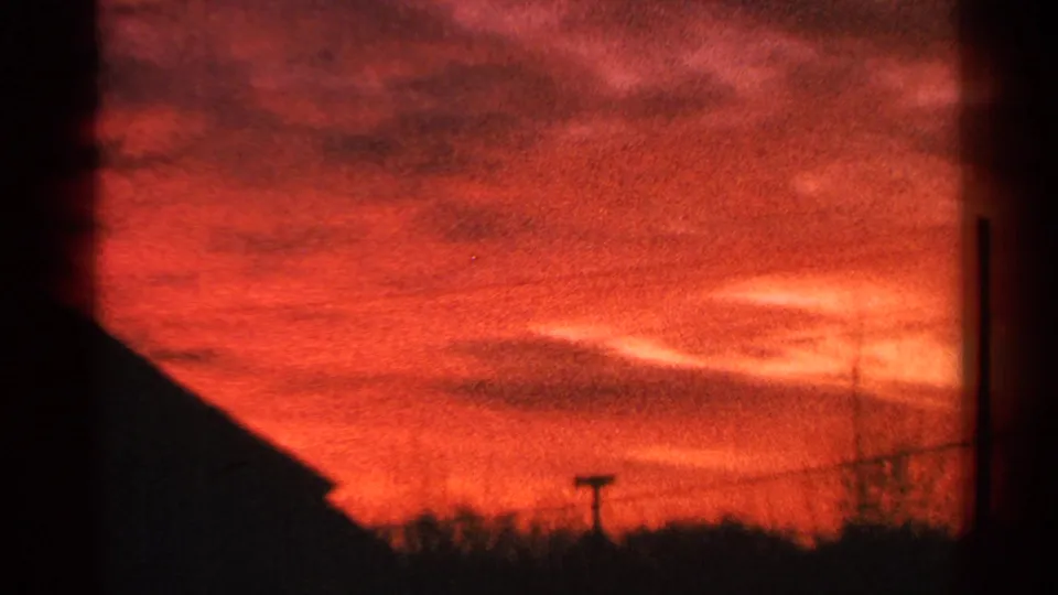 1964 Milwaukee 8mm frame showing a red sunset over a low roofline, utility wires, bare trees, and a small pole silhouette.