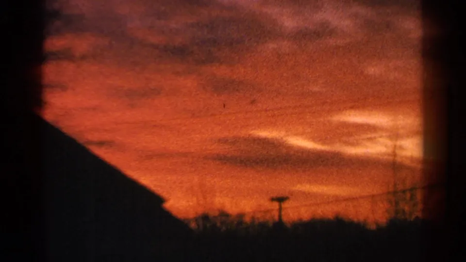 1964 Milwaukee 8mm view of a red-orange sunset with a roof silhouette, utility pole, and faint branches along the horizon.