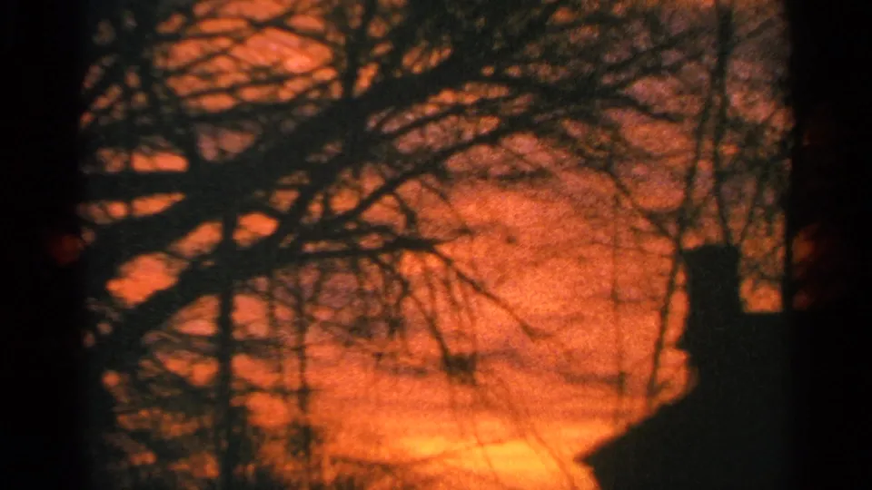 1964 Milwaukee 8mm frame showing bare tree limbs and a chimney shape silhouetted against a glowing sunset sky.